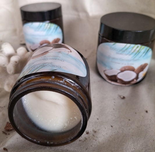 three amber jars of organic coconut balm with tropical labels, showcasing smooth, white balm inside one open jar, placed on a natural fabric background.