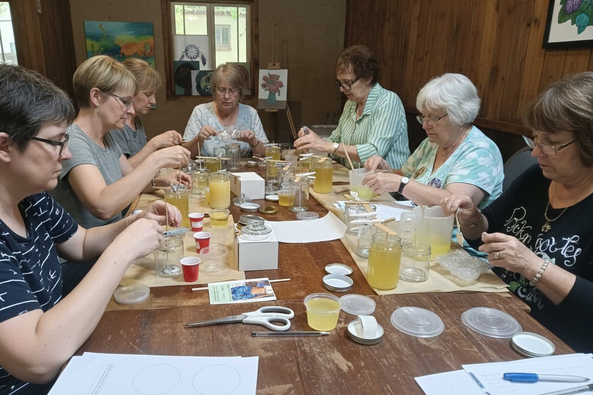 Group of people at a table with art supplies and drinks, possibly in an art class or workshop, 