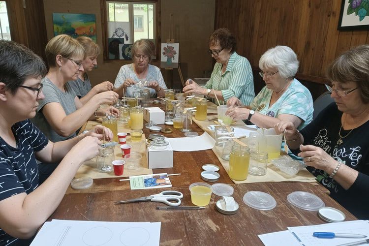 Group of people at a table with art supplies and drinks, possibly in an art class or workshop, 