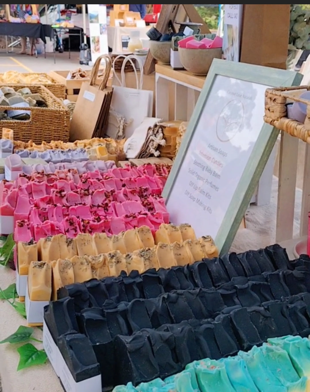 A variety of handmade soaps displayed on a table at a market. The soaps are in different colors and shapes, including pink, yellow, orange, black, and blue.

handmade soap, natural soap, organic soap, variety pack, bath and body products, skincare
